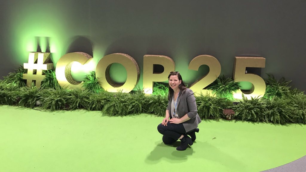 Kate O'Neill squats in front of a #COP25 sign